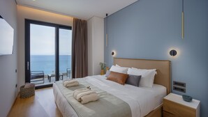 A modern hotel room with a large bed, a nightstand, a bedside table, and a view of the sea through a sliding glass door. - Villa Nereid 5 bedroom villa with infinity heated pool (Rodia)