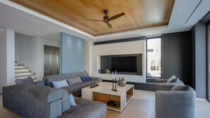A modern living room with a grey sectional sofa, a coffee table, and a flat-screen TV mounted on the wall. - Villa Nereid 5 bedroom villa with infinity heated pool (Rodia)
