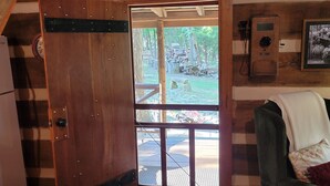 L’intérieur d’un chalet rustique, avec une porte en bois donnant sur un espace extérieur, un banc en bois, un canapé et un radiateur fixé au mur.