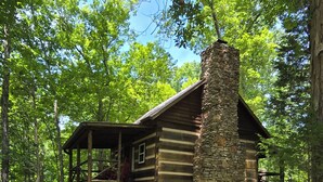 Un chalet rustique en rondins de bois, doté d’une cheminée en pierre, entouré d’un sentier pavé et d’une végétation luxuriante.