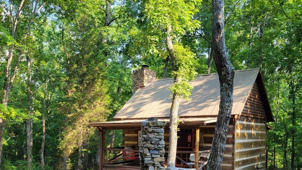 Un chalet rustique avec une cheminée en pierre, entouré d’une forêt.