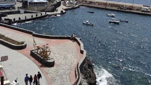 Un pueblo costero con un puerto deportivo, paseos empedrados y edificios a lo largo del litoral.