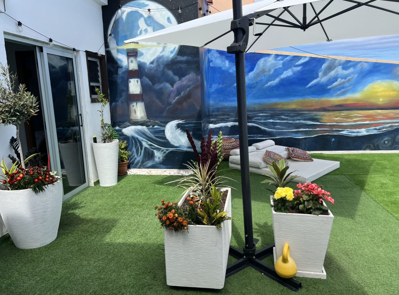 A rooftop garden with artificial grass, potted plants, and a mural of a lighthouse and ocean scene.
