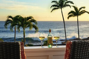 A seaside view with two wicker chairs, a table with a bottle and glasses of white wine, and palm trees. - Hale Pohaku Kai: Poipu Seaside Stunner (Koloa)