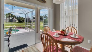 Zona pranzo con tavolo imbandito per quattro, vista su un giardino con piscina e un'ampia finestra con tende.