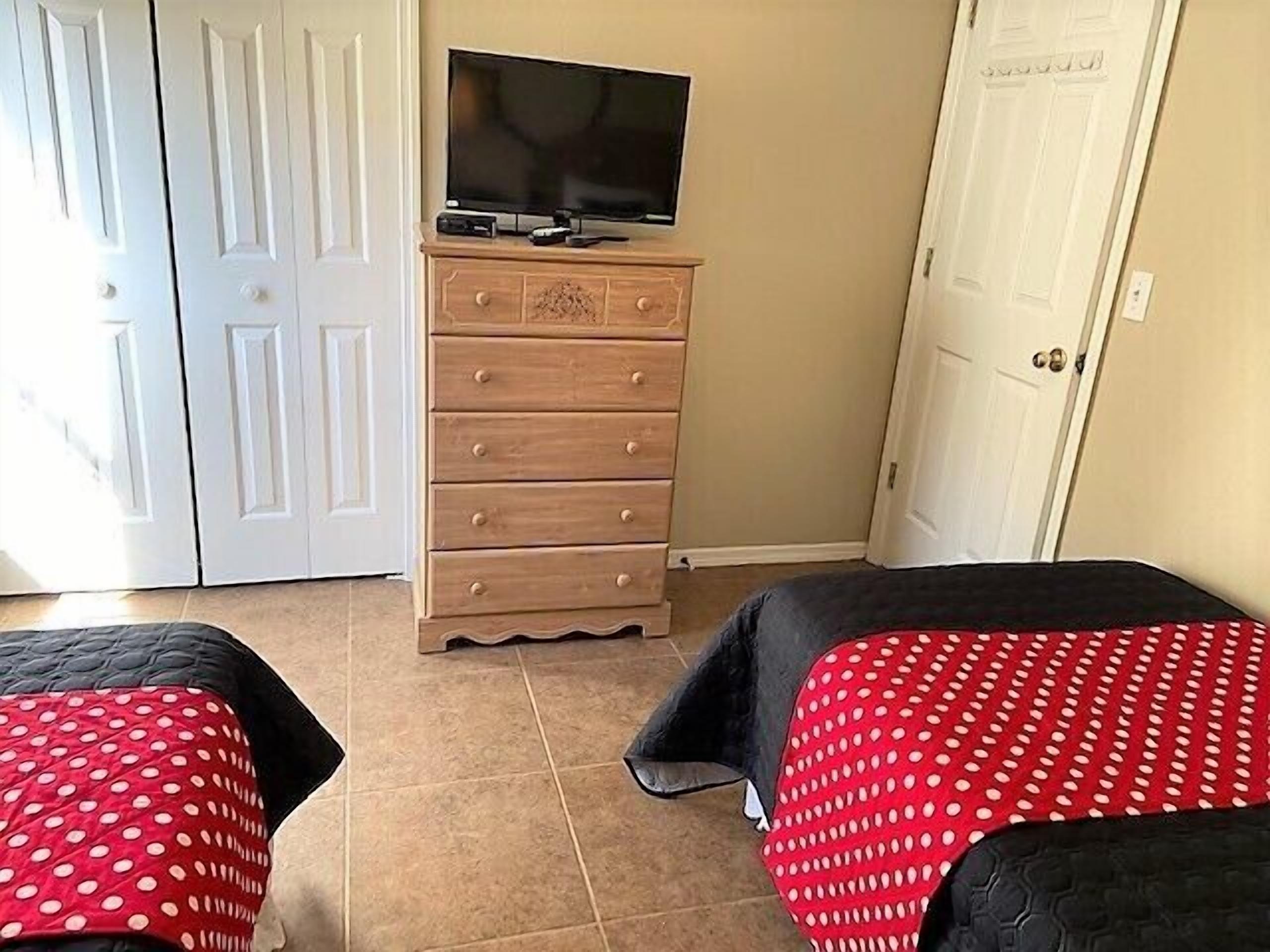 A room with two beds, a dresser, a television on top, and two white doors.
