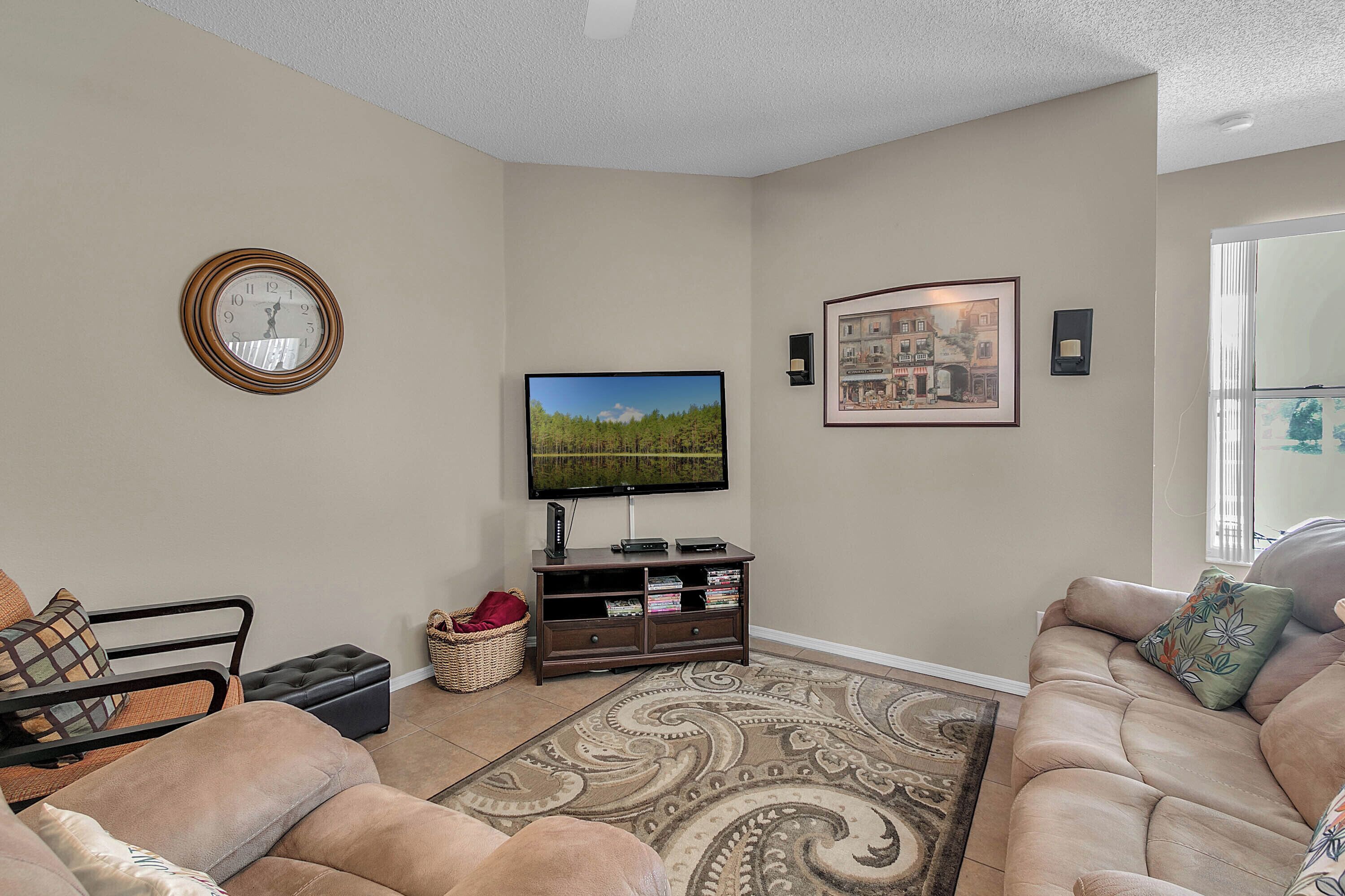 A living room with a sofa, a television, a clock, and a framed picture on the wall.