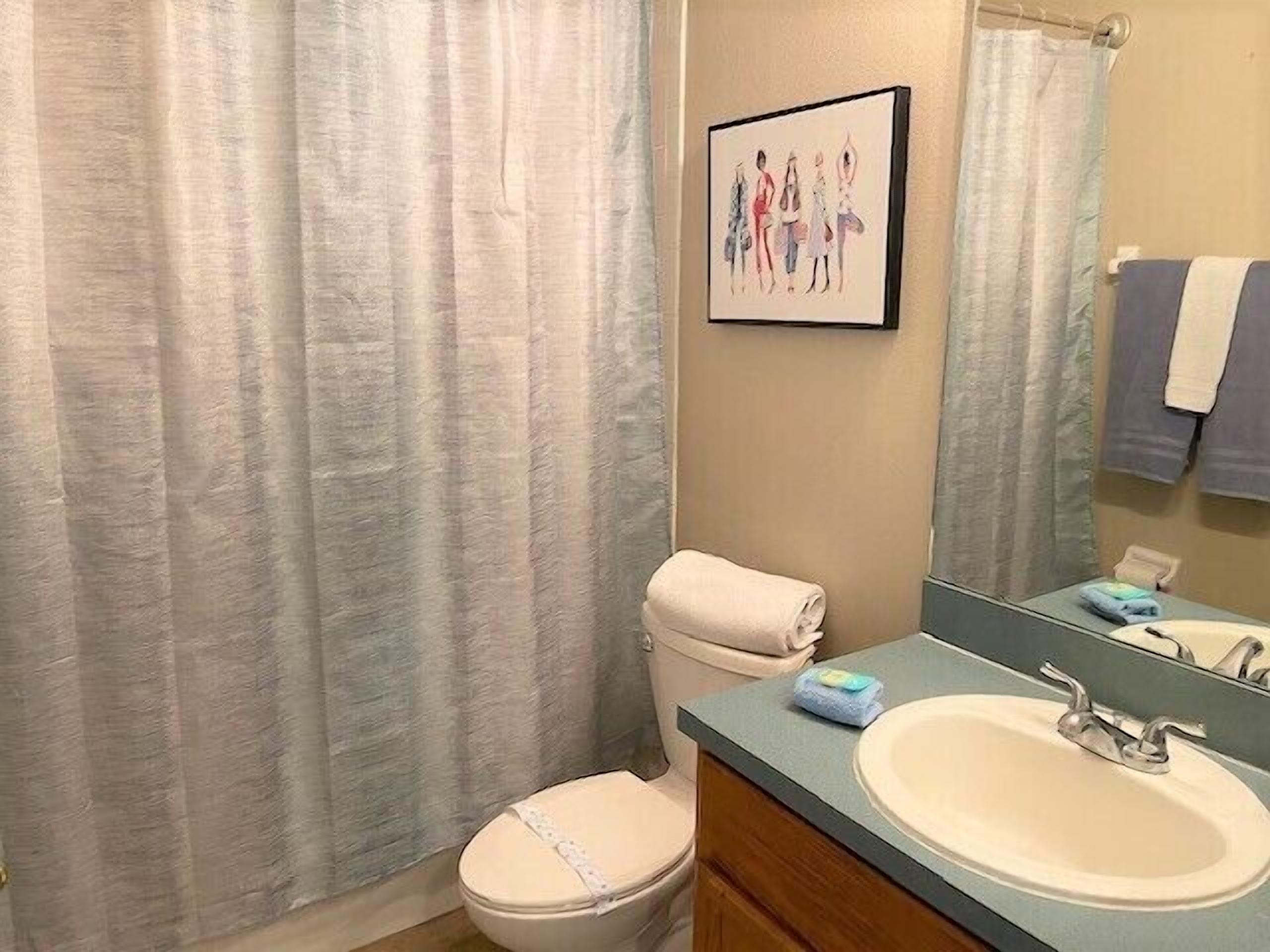 Un baño con inodoro, lavabo, espejo y un cuadro en la pared.
