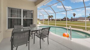 Una terrazza esterna con tavolo e sedie in vetro, una piscina e vista su una zona residenziale.