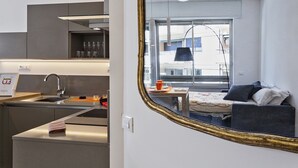 A compact kitchen with modern appliances, a dining area with a table and chairs, and a large mirror reflecting a bedroom with a bed and window. - Studio Piccolo a Carignano by Wonderful Italy (Genoa)