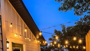 Una casa con puerta verde, un banco de madera y luces colgantes.