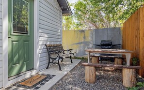 Eine Terrasse mit einer Bank, einem Picknicktisch, einem Grill und einer Tür mit grünem Rahmen.