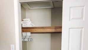 Un armario abierto con un estante de madera, una percha y un taburete pequeño.