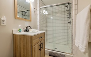 A bathroom with a wooden vanity, a mirror, a sink, a shower with a glass door, and a towel rack. - Downtown Casita- Charming one bedroom, close to Downtown Cody (Cody)