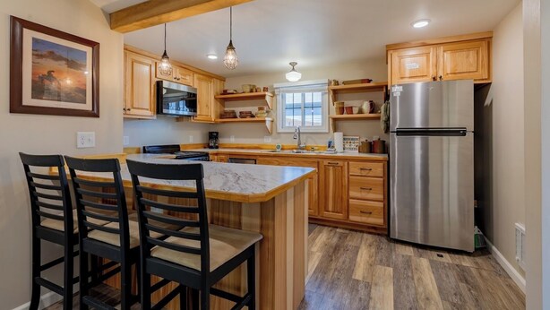 Una cocina con armarios de madera, un refrigerador de acero inoxidable, una isla de mármol e iluminación colgante.