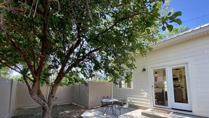 Un jardin avec un arbre, une table de patio et une porte-fenêtre coulissante donnant sur la cuisine.
