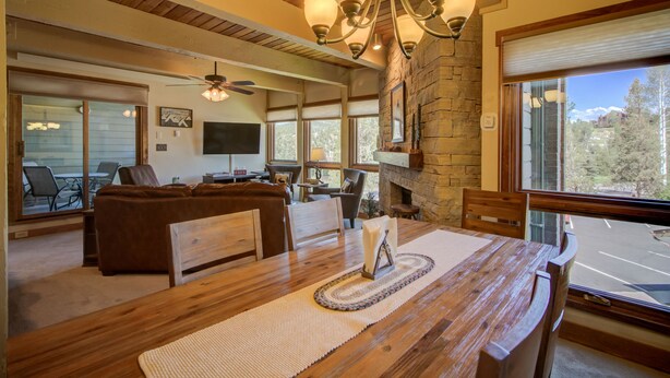 A spacious living area with a fireplace, wooden furniture, and large windows offering a view of the outdoors. - 2BR Condo | Walk to Gondola | Pool, Hot Tubs and Fireplace! (Steamboat Springs)