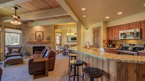 A spacious living area with a fireplace, a stone wall, and a large wooden ceiling. - 2BR Condo | Walk to Gondola | Pool, Hot Tubs and Fireplace! (Steamboat Springs)