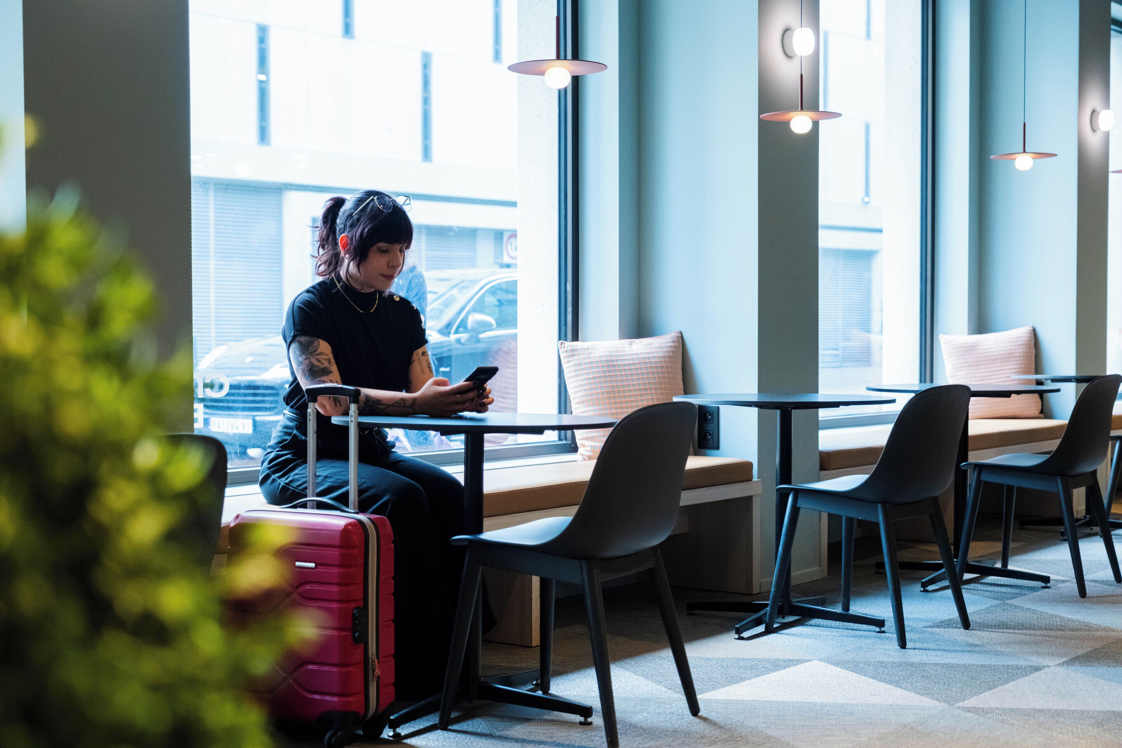 A person sitting at a table with a laptop, a suitcase, and a window view of a building and street.