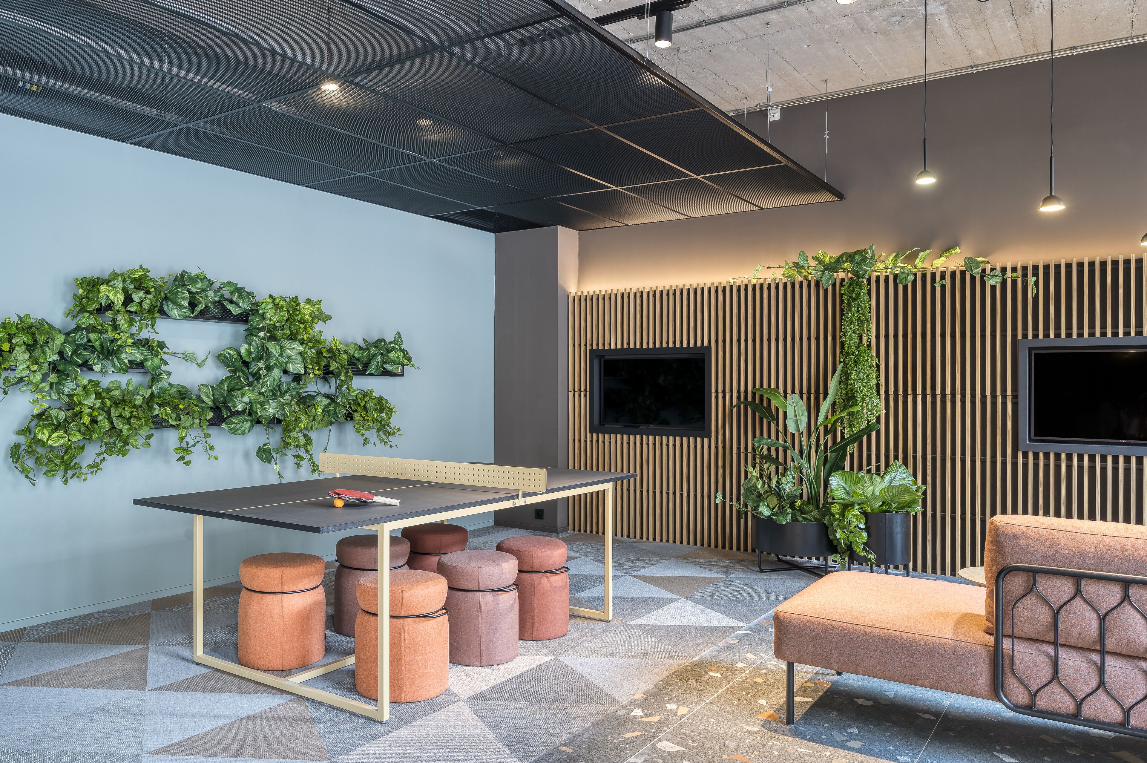 Un espace de bureau moderne avec une longue table, de nombreux tabourets, un canapé et des plantes vertes.