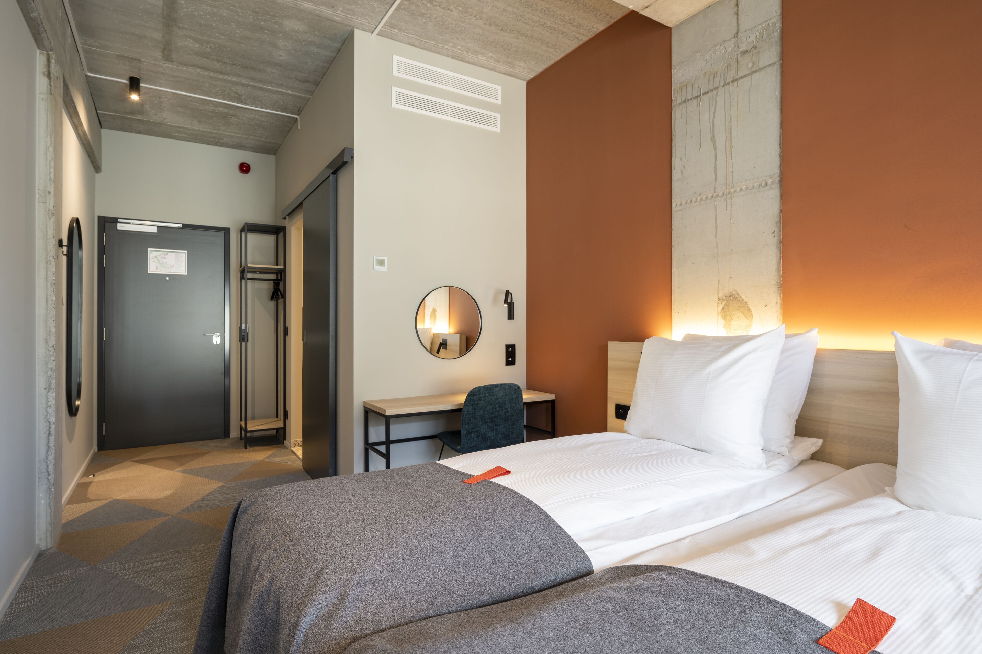 A hotel room with a large bed, a desk, a chair, and a mirror.