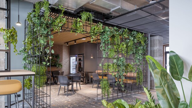 Espacio interior con diseño moderno, que presenta una pared de ladrillo, estructuras metálicas con vegetación y una variedad de arreglos de asientos.