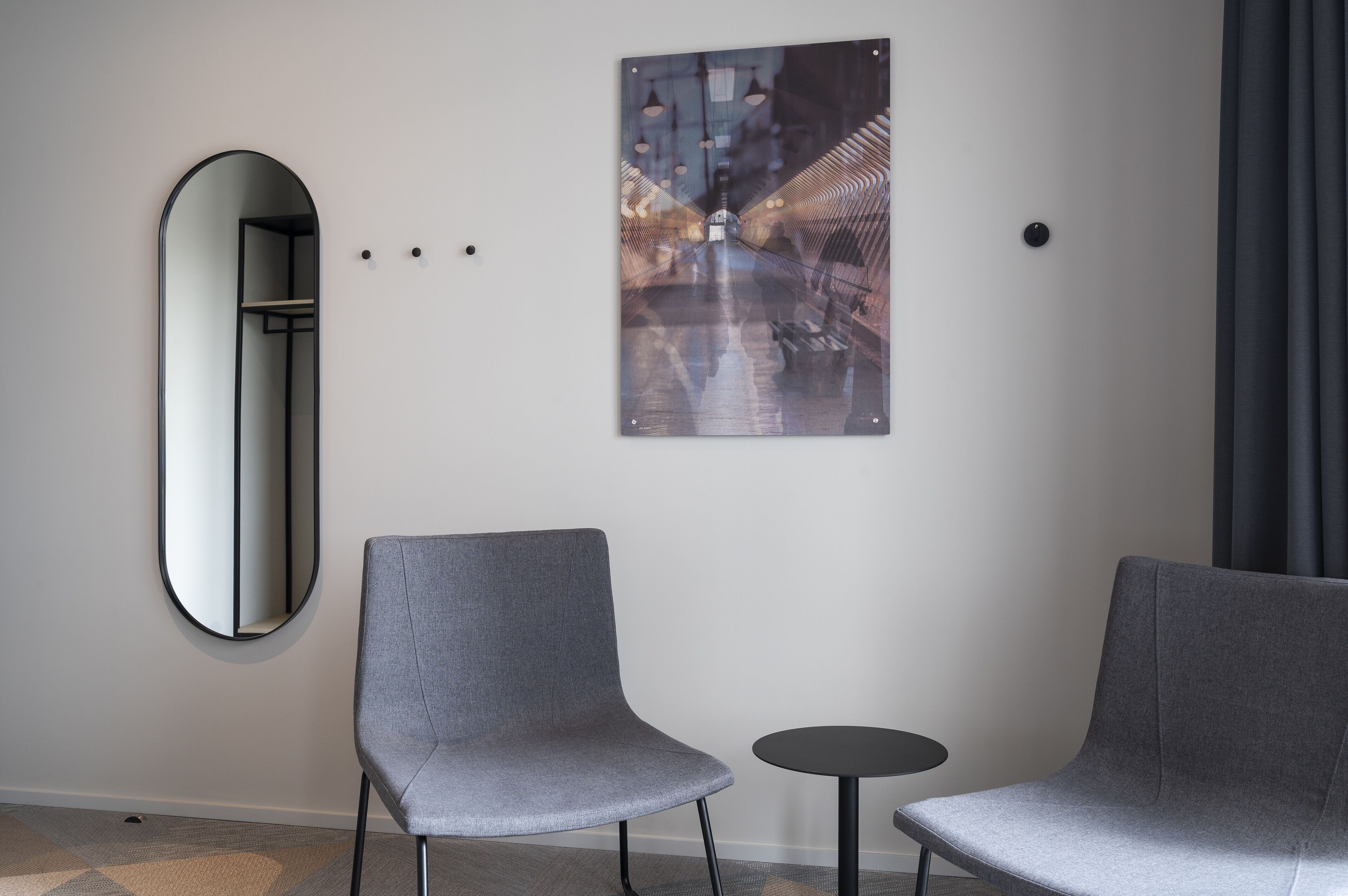 Una habitación moderna con dos sillas grises, una pequeña mesa redonda y un cuadro abstracto grande en la pared.