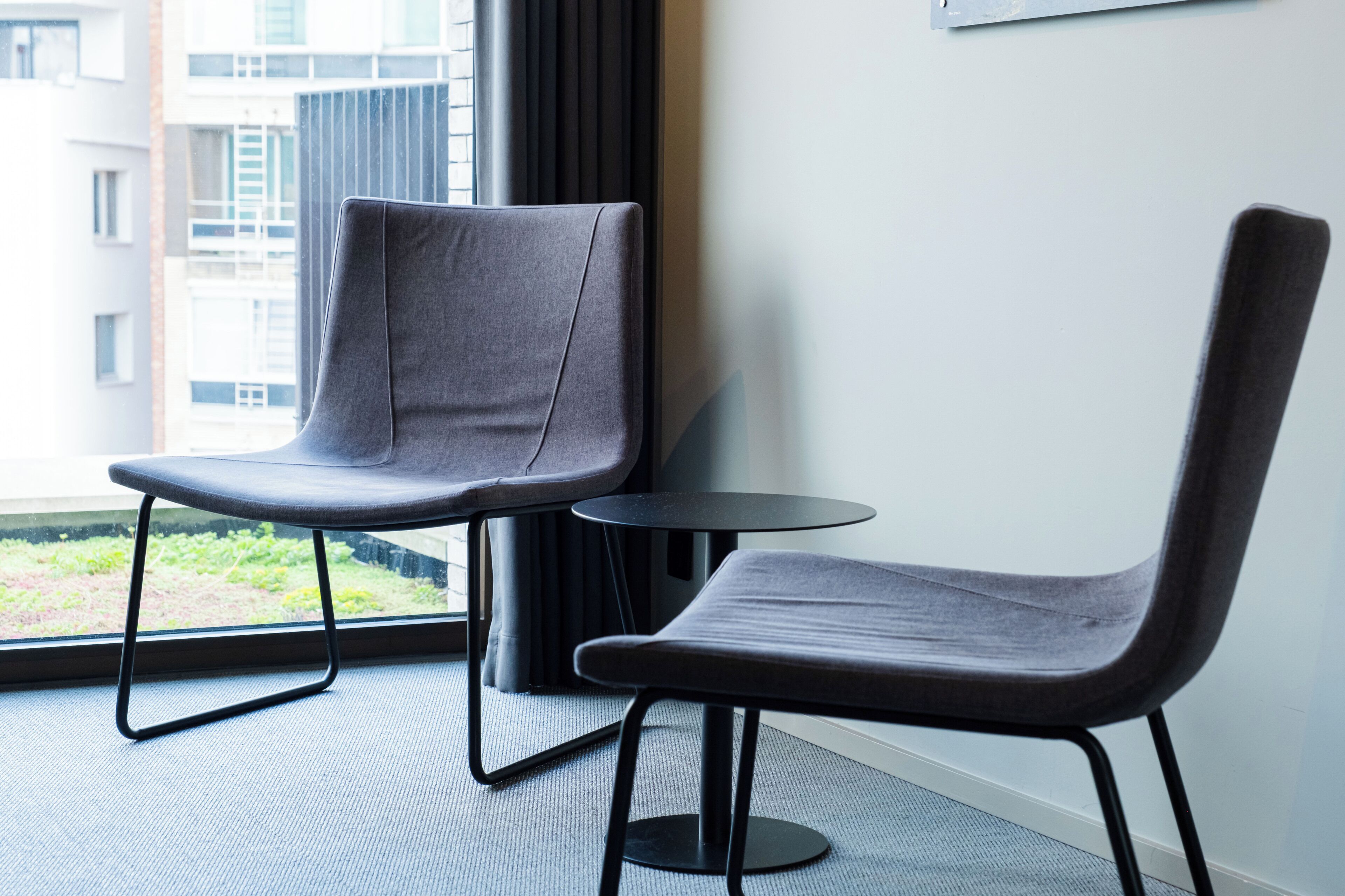 Two grey chairs with metal frames and a small round table in a room with a large window.