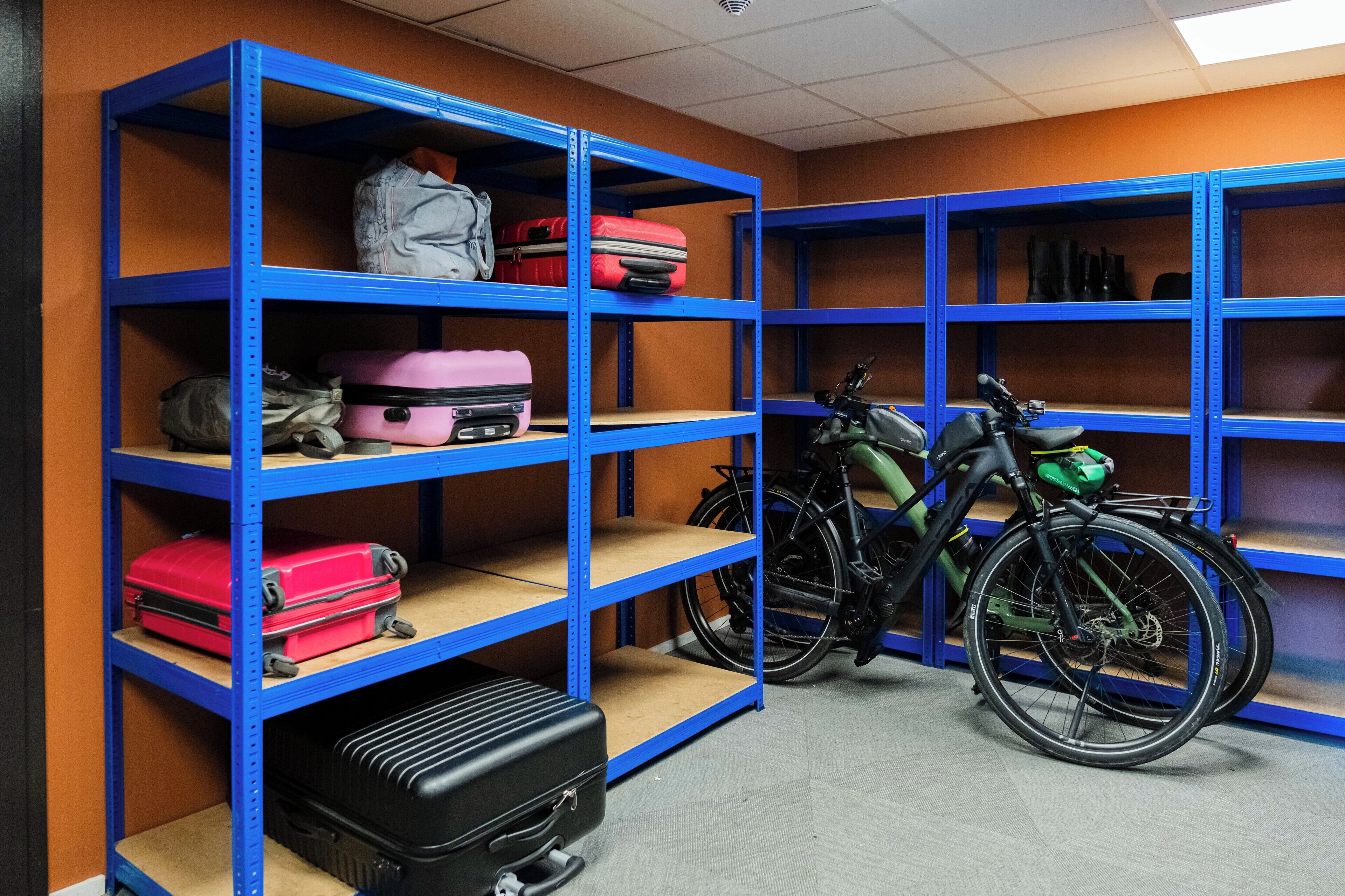 Un espacio de almacenamiento con estanterías azules que contienen maletas y una bicicleta.
