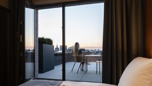 Un dormitorio con un amplio ventanal corredera que da a un balcón con vistas a la ciudad.