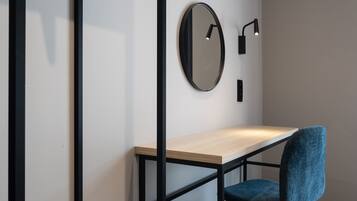 Une chambre moderne avec un bureau en bois, une chaise bleue, un miroir rond et un luminaire fixé au mur.