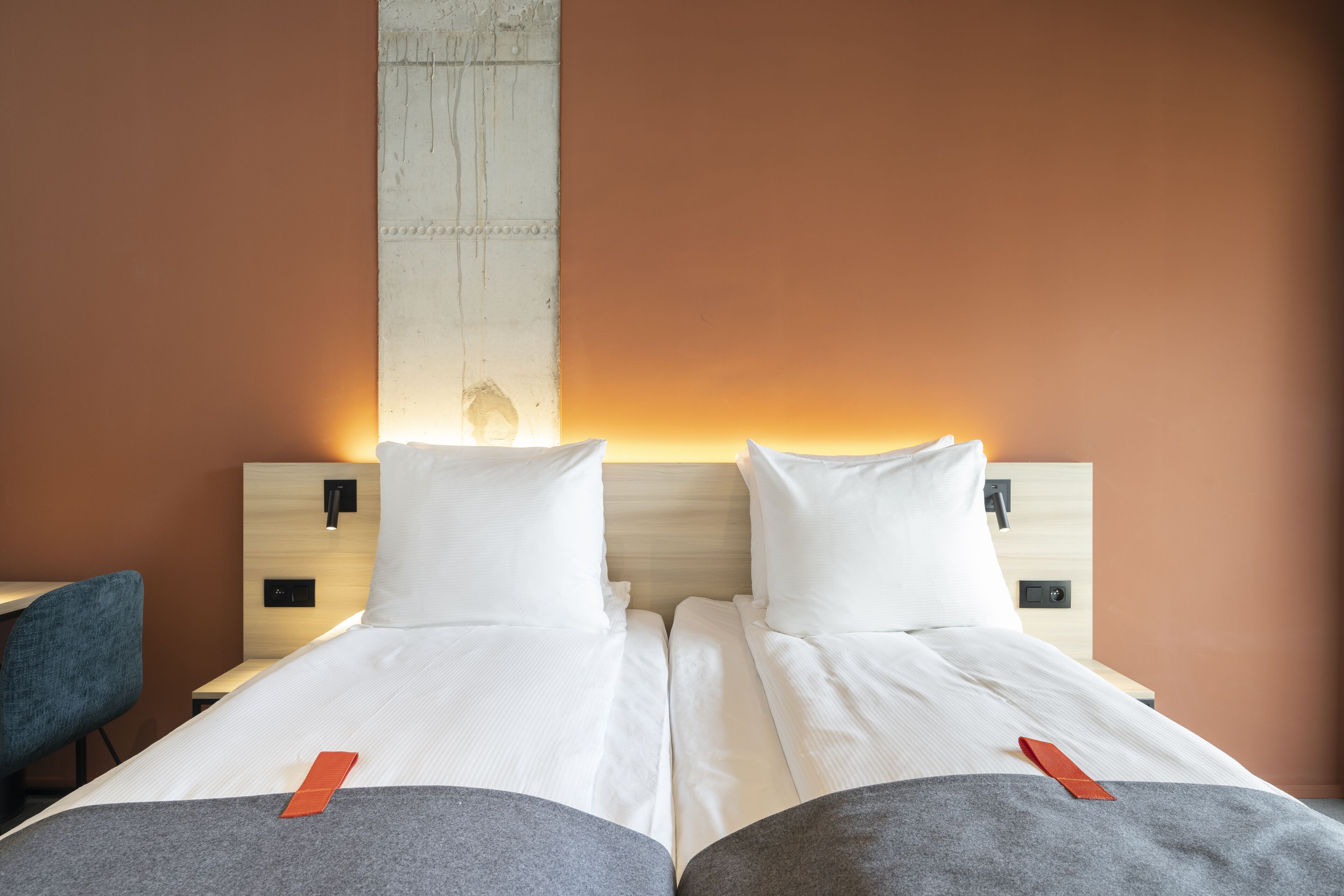 Een tweepersoonsbed met wit beddengoed en twee kussens, een houten hoofdbord en een nachtkastje met een lamp.