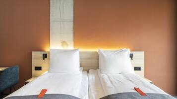 Een tweepersoonsbed met wit beddengoed en twee kussens, een houten hoofdbord en een nachtkastje met een lamp.