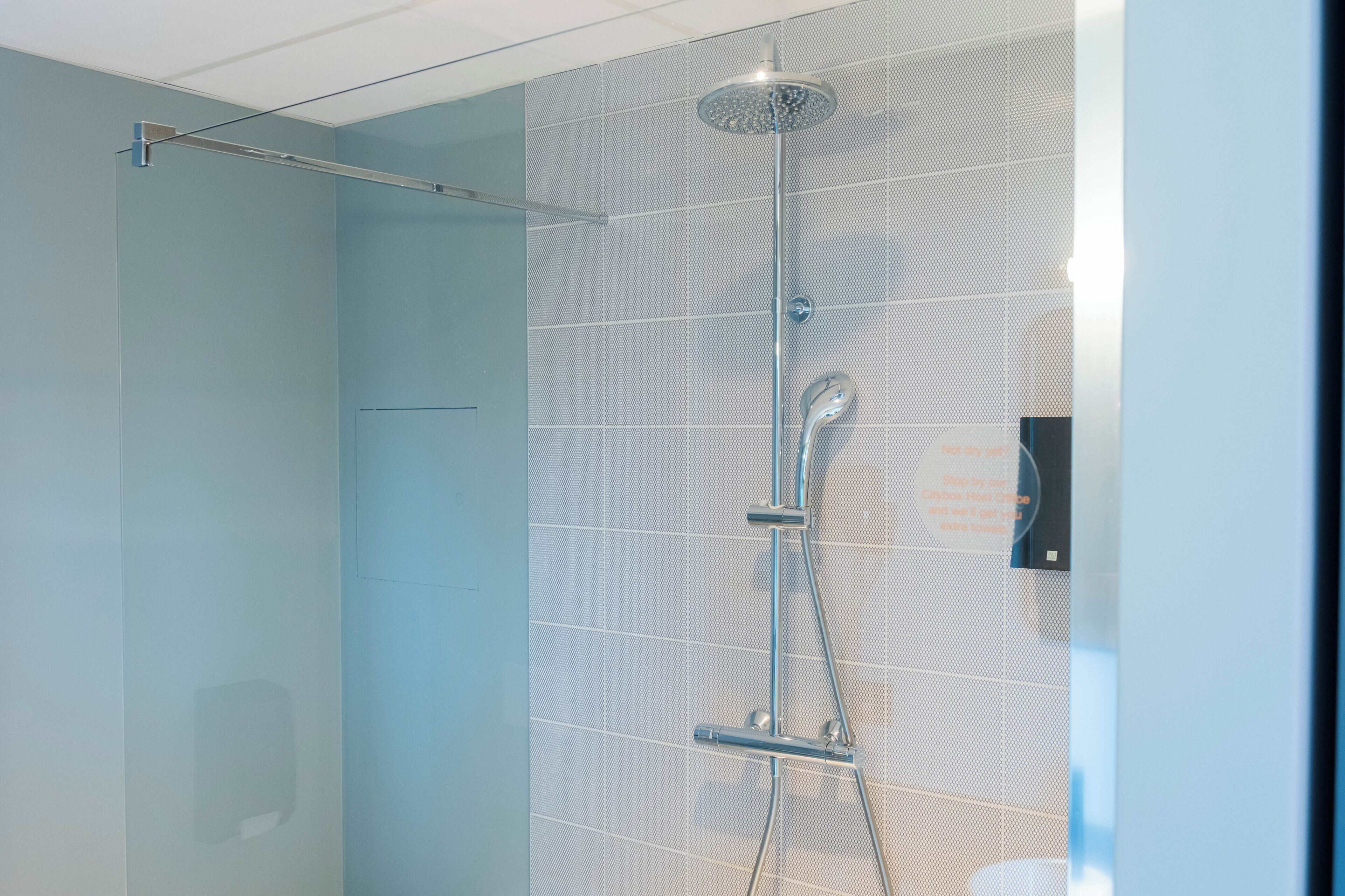 A modern shower with a rain showerhead and handheld showerhead, a glass partition, and a control panel on the wall.