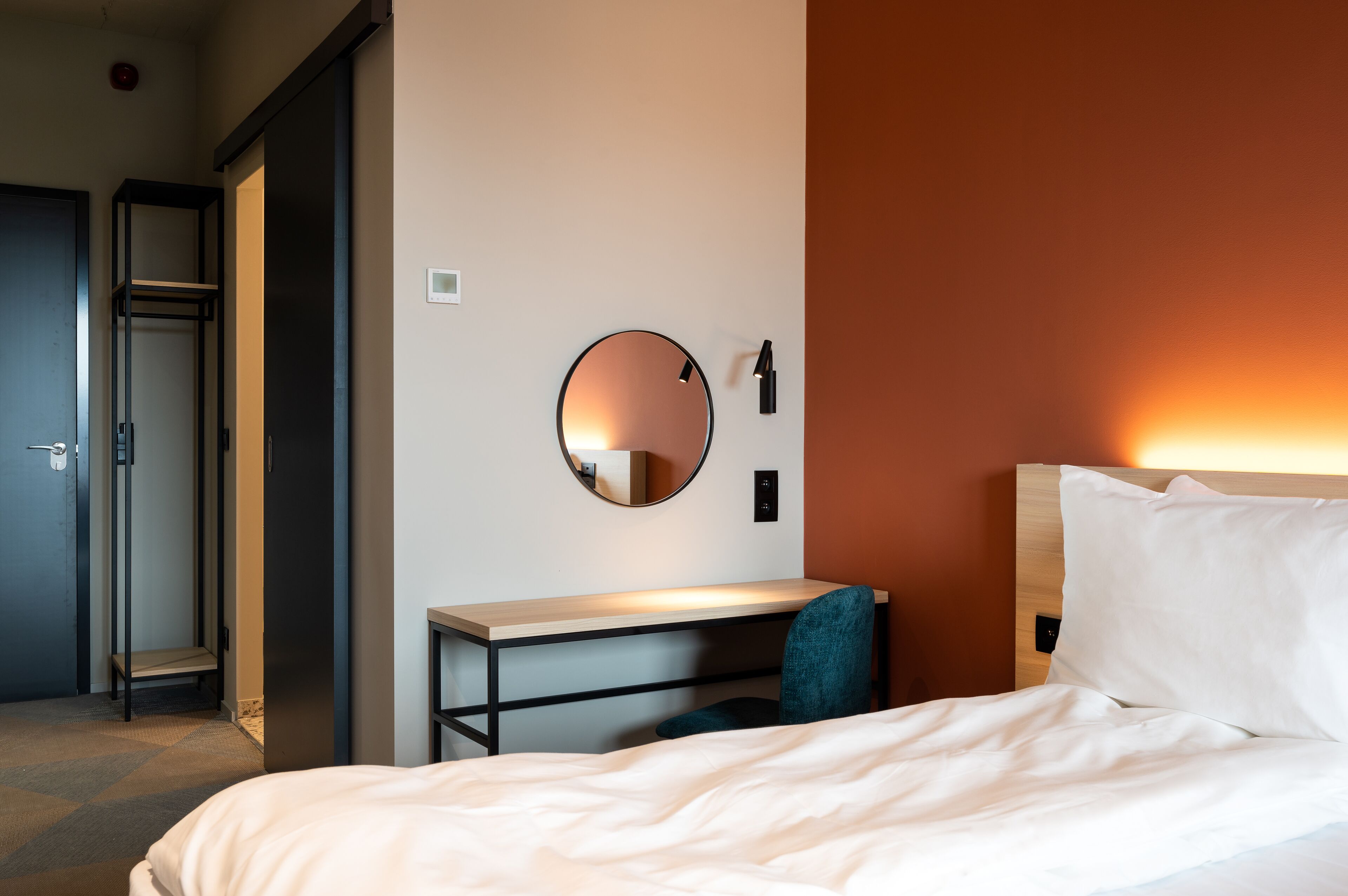 Une chambre d’hôtel comprenant un lit, un bureau, une chaise, un miroir rond et une armoire.