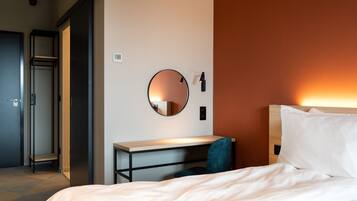 Een hotelkamer met een bed, een bureau, een stoel, een ronde spiegel en een kledingkast.