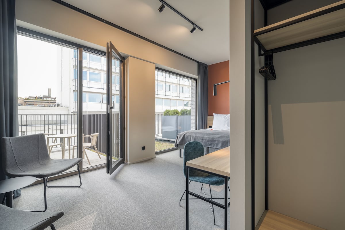 Een moderne hotelkamer met balkon, een bed, bureau en stoel.