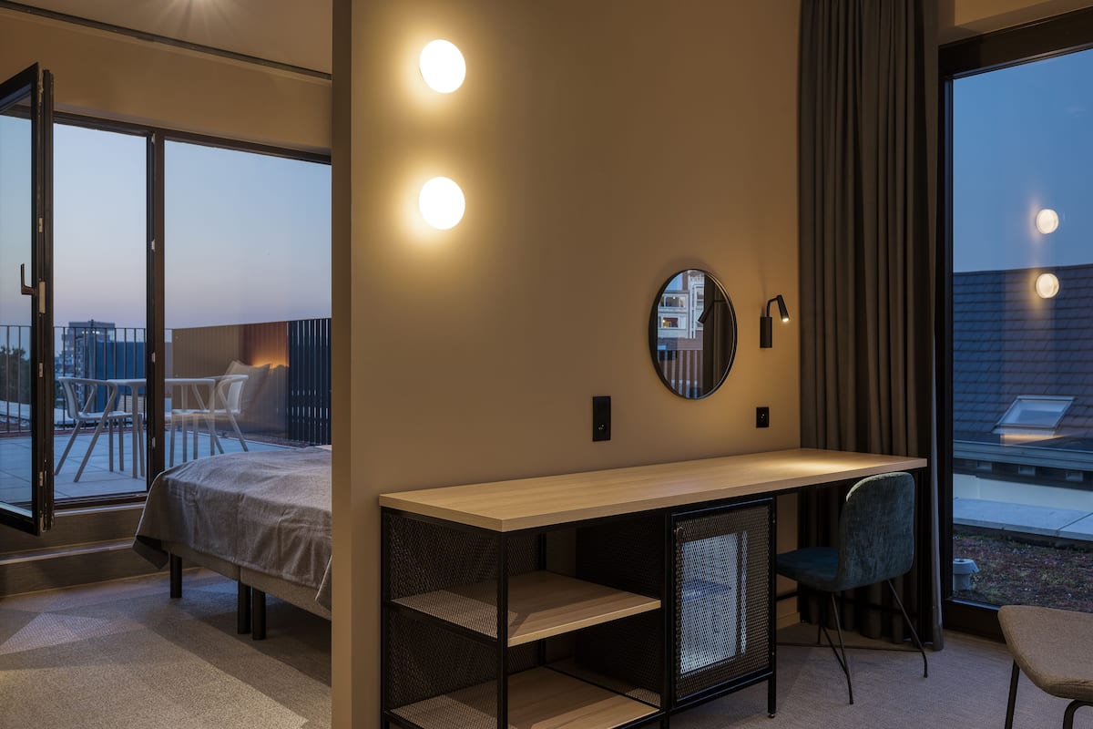 Een moderne hotelkamer met een bed, een bureau, een stoel en een groot raam met uitzicht op de stadszicht.