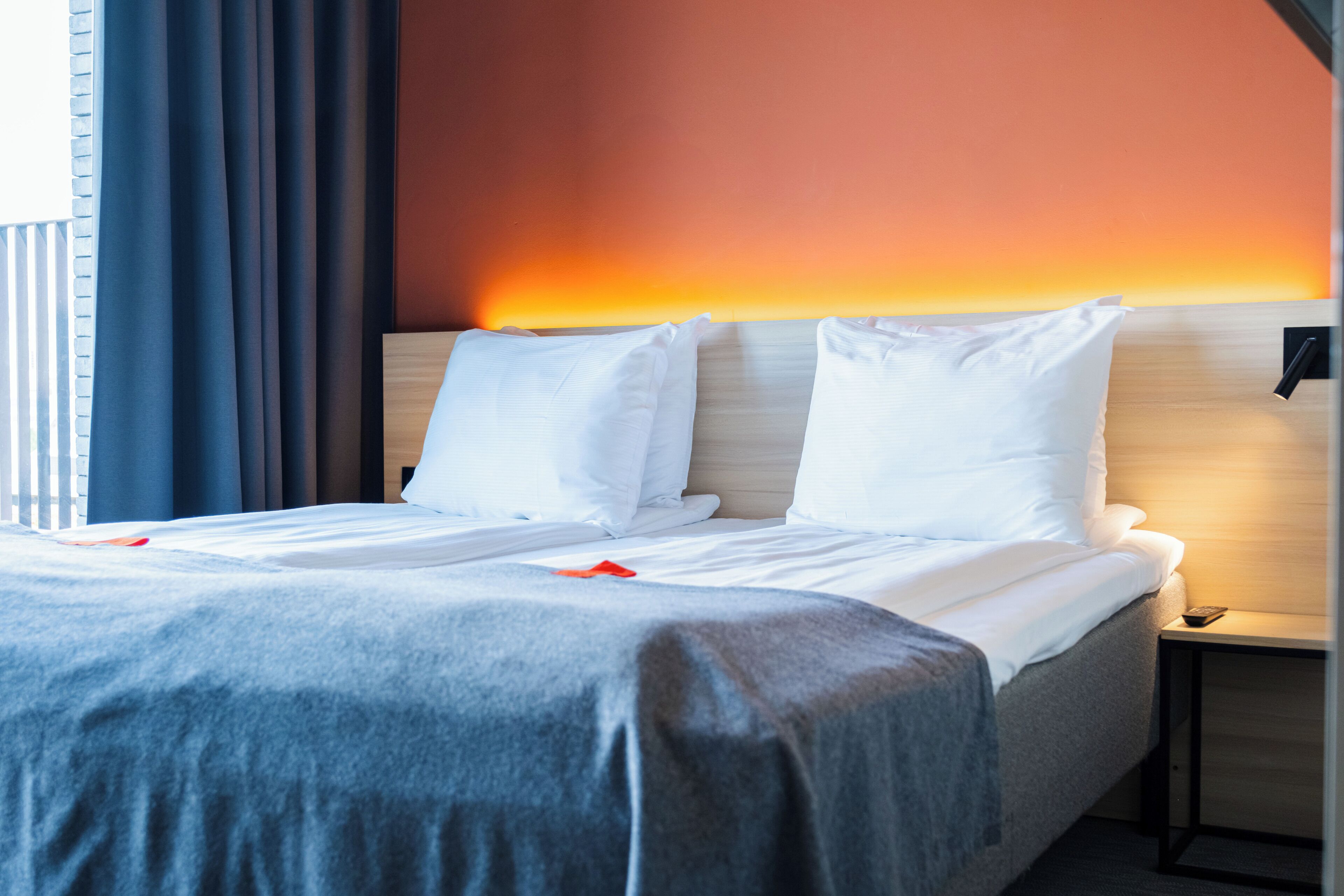 A neatly made bed with white linens, a grey blanket, and a wooden headboard.