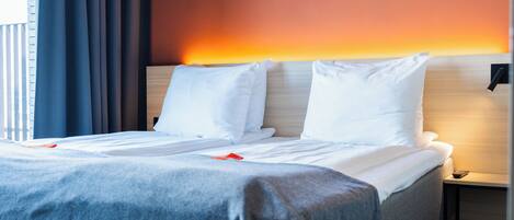 A neatly made bed with white linens, a grey blanket, and a wooden headboard.