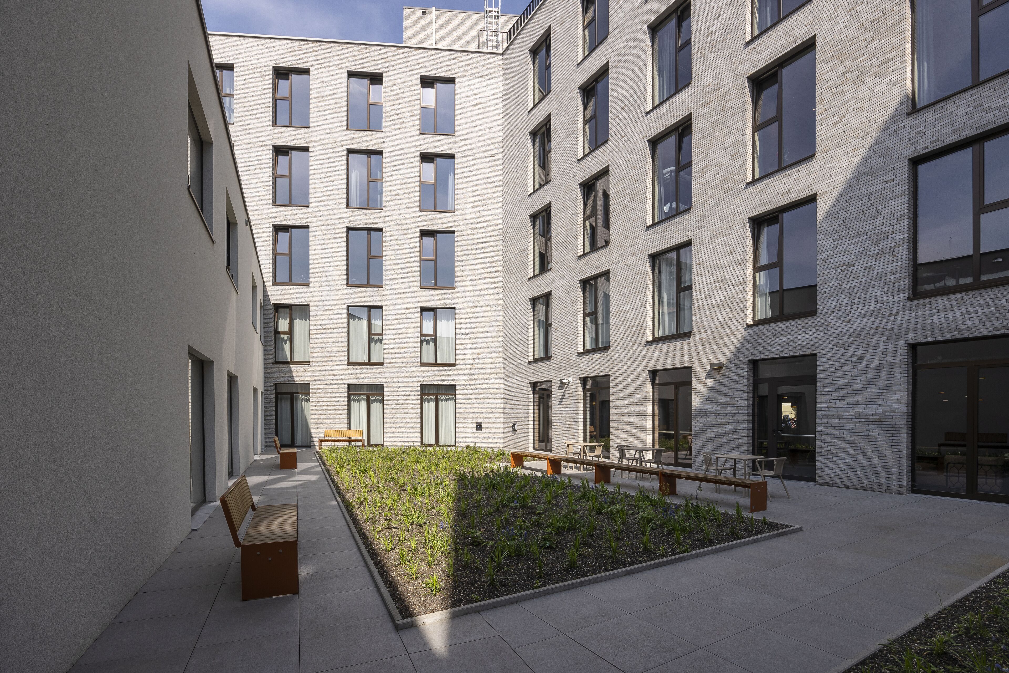 A courtyard with a central garden, benches, and a building with multiple windows and doors.