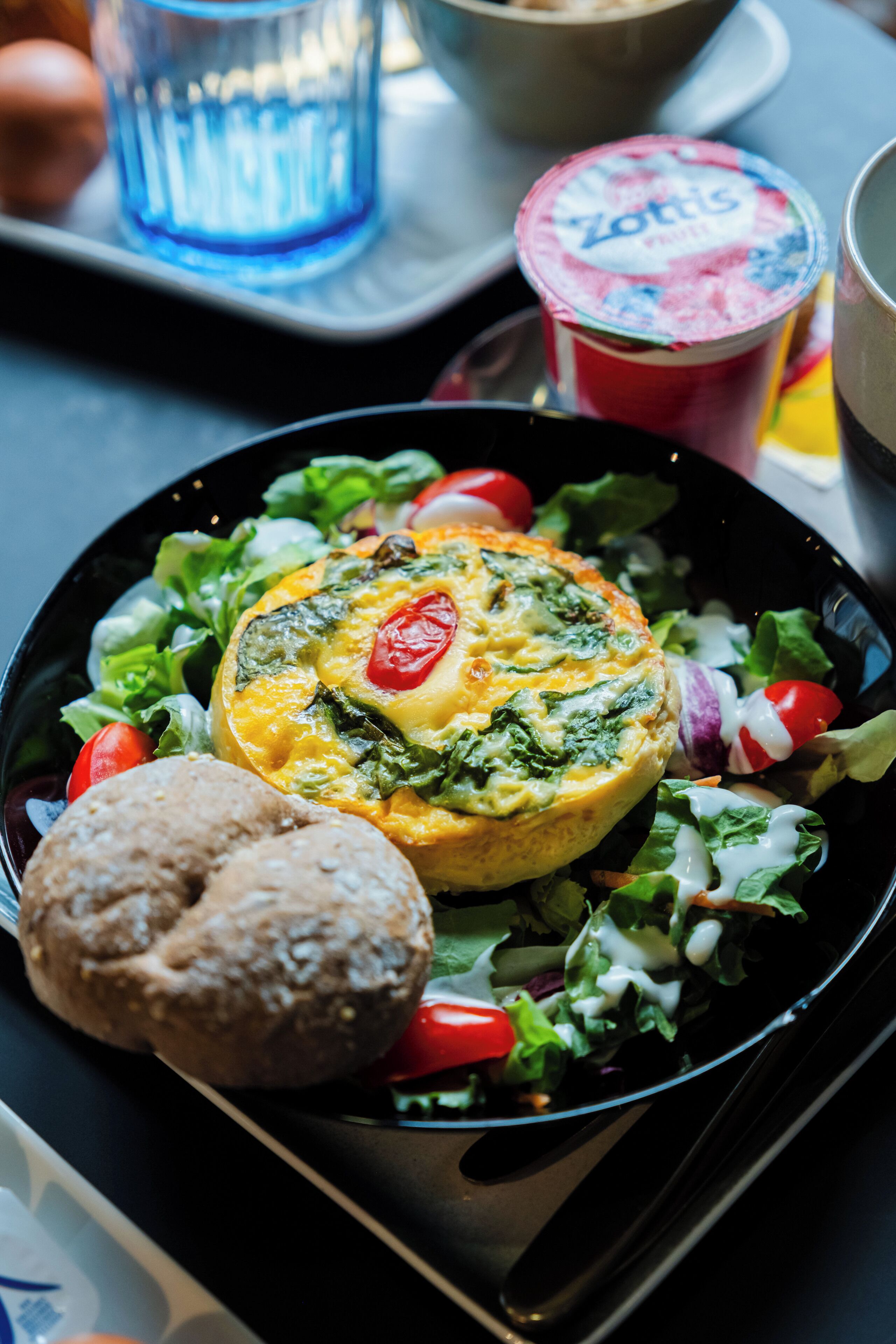 Un repas composé d’une salade agrémentée d’un œuf cuit au four, de tomates cerises et d’un muffin, le tout présenté dans une assiette noire.