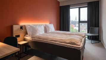 Une chambre d’hôtel avec un lit, un bureau, une chaise et une grande fenêtre donnant sur la ville.