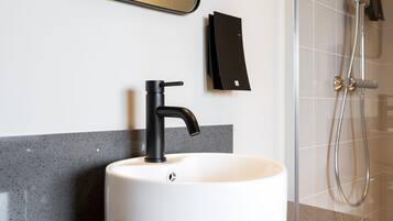 Un baño moderno con lavamanos blanco, grifo negro y zona de ducha.