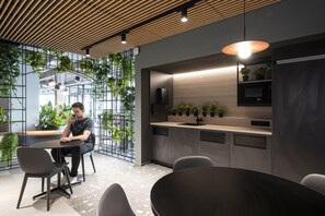 A modern kitchen with built-in appliances, a dining area with chairs, and a person sitting at a table. - Citybox Antwerp City Center (Antwerp)