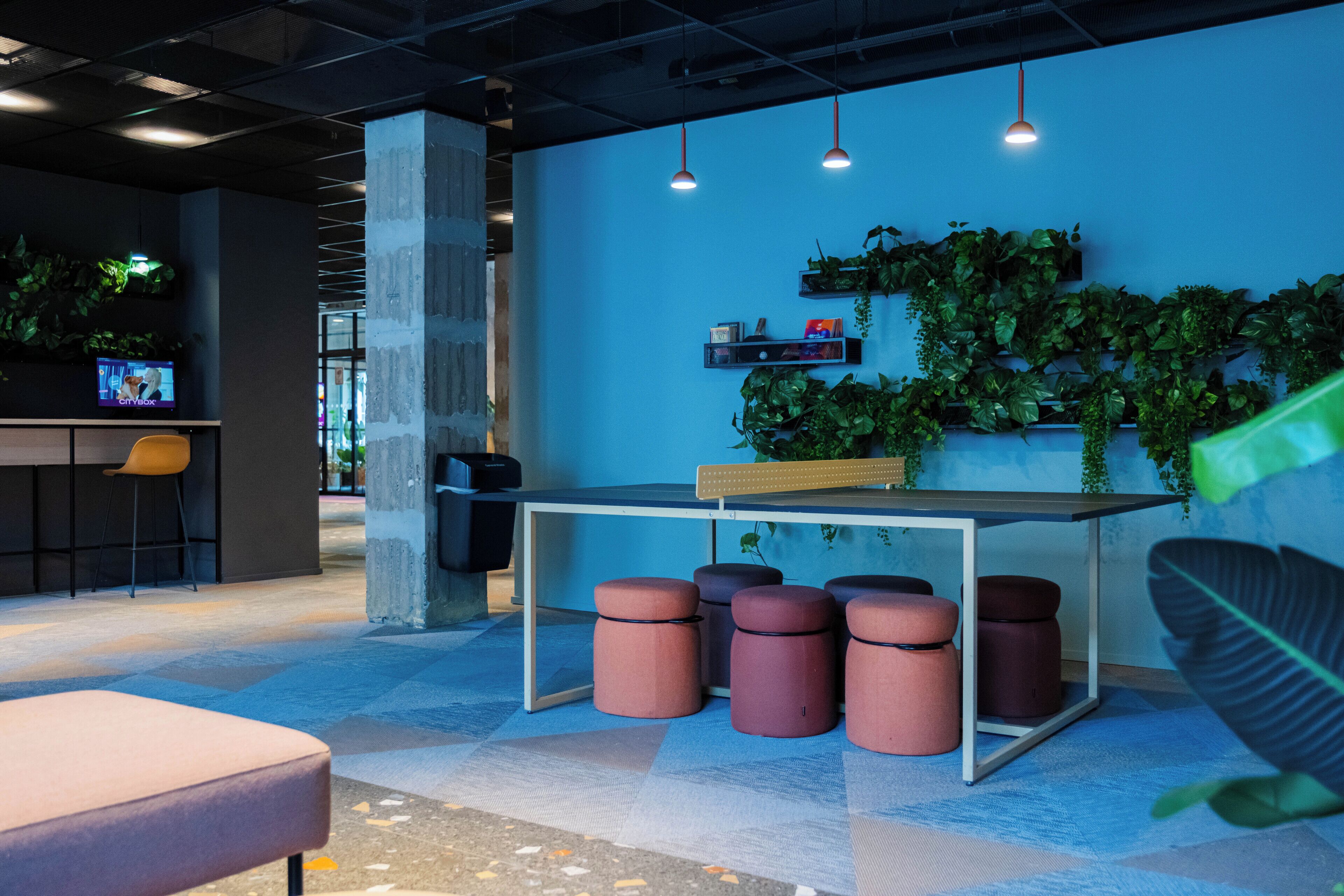 Un espace de bureau moderne avec un mur d’accent bleu, un coin bar et un aménagement avec des tabourets et des poufs.