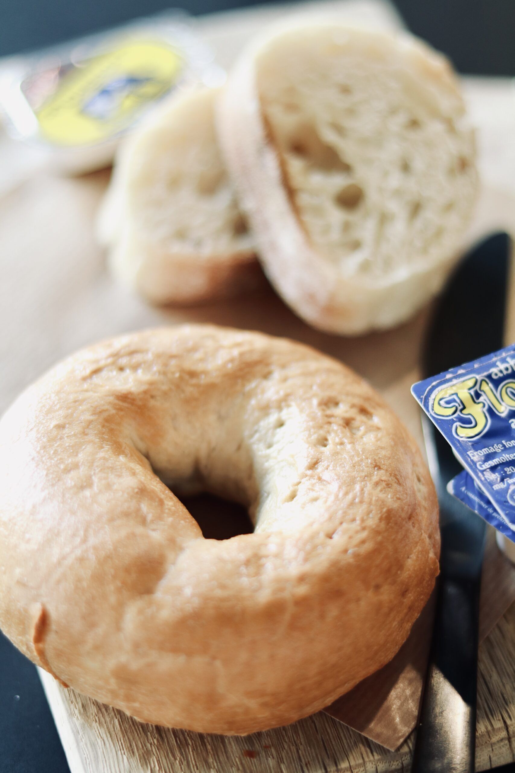 Un bagel sobre tabla de madera con un cuchillo y un paquete de queso crema.