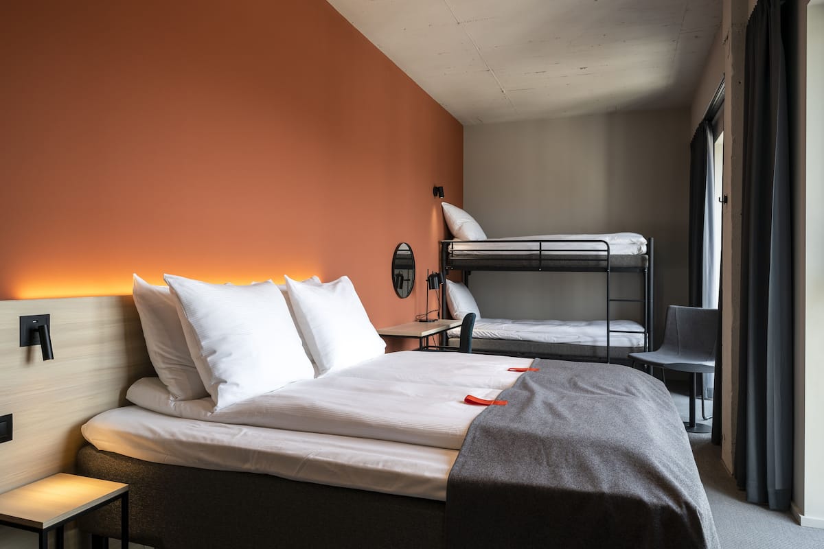Een hotelkamer met een stapelbed, een eenpersoonsbed, een bureau, een stoel en een nachtkastje.