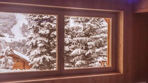 Una cabaña de madera con un amplio ventanal que da a un bosque nevado.