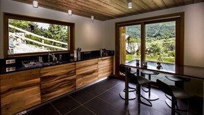 Una cocina moderna con armarios de madera, encimera negra y vistas a un paisaje montañoso a través de amplios ventanales.